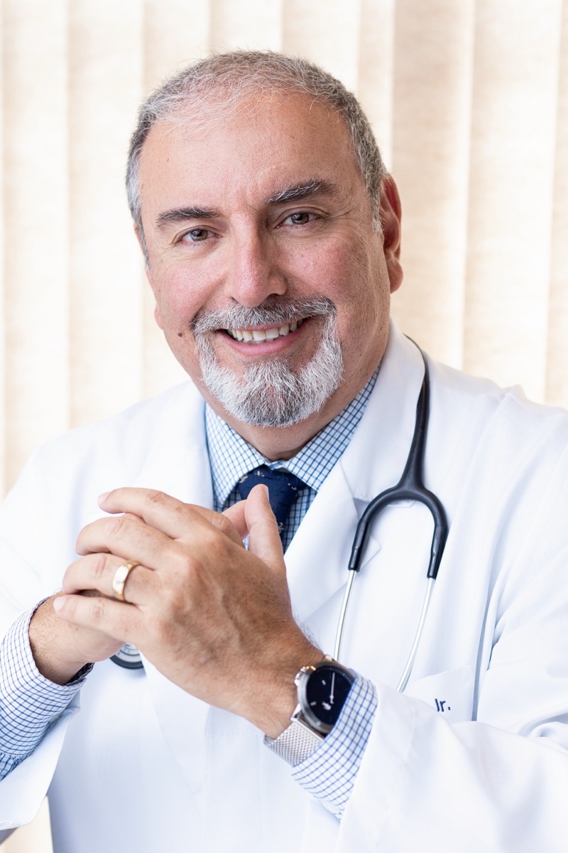 Retrato em consultório, com jaleco e estetoscópio.